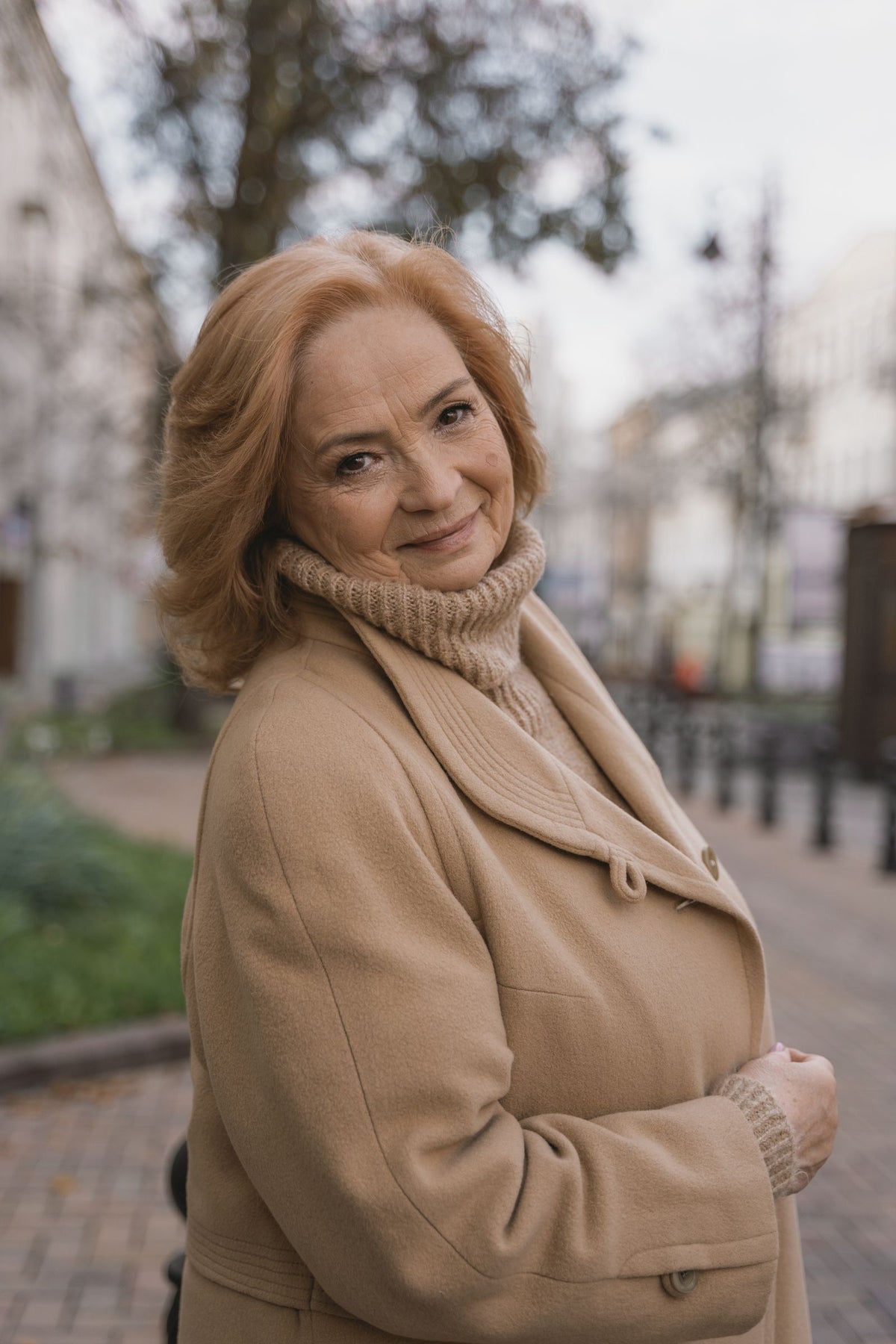 Smiling woman in a camel coat outdoors in fall